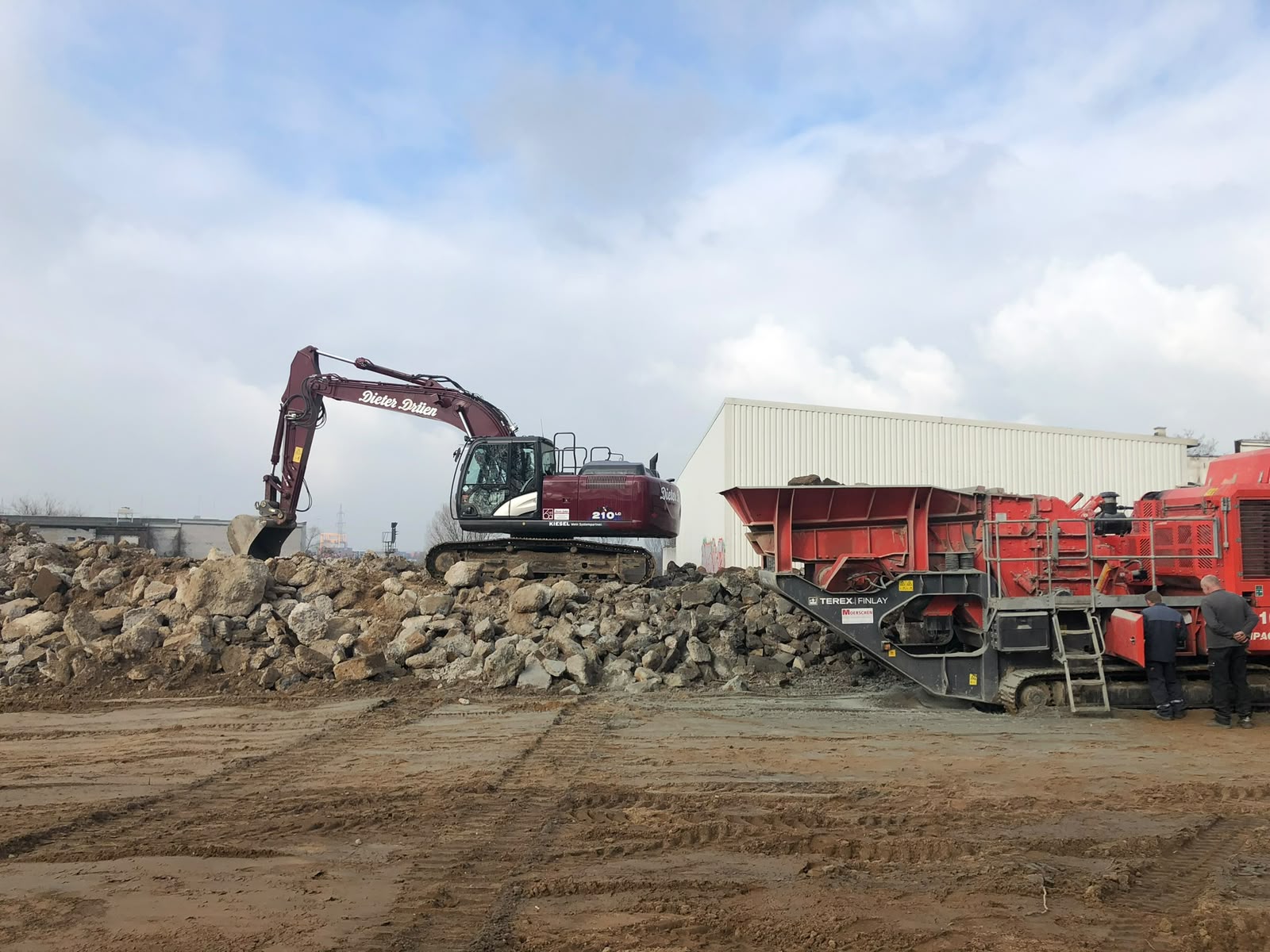 Mobile Brechanlage recycelt Bauschutt neben einem Kettenbagger